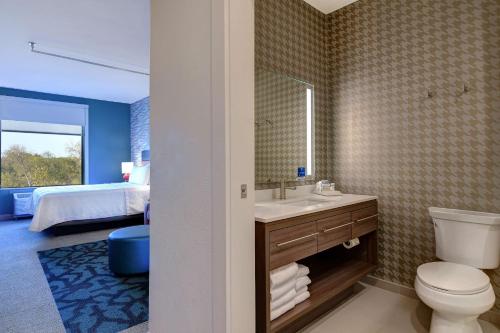 a bathroom with a toilet and a sink and a bed at Home2 Suites by Hilton North Plano Hwy 75 in Plano