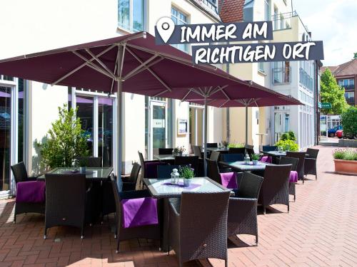 un restaurant en plein air avec des tables et des chaises sous des parasols dans l'établissement ACHAT Hotel Buchholz Hamburg, à Buchholz in der Nordheide