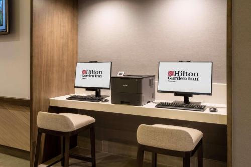 two computer monitors sitting on a counter with two chairs at Hilton Garden Inn Chino Hills Pomona CA in Pomona