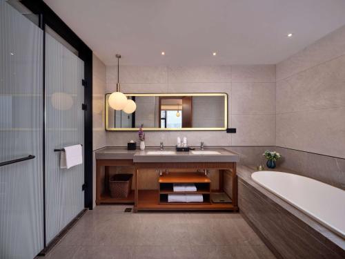 a bathroom with a sink and a tub and a mirror at Hilton Garden Inn Jinzhou Central Street in Jinzhou