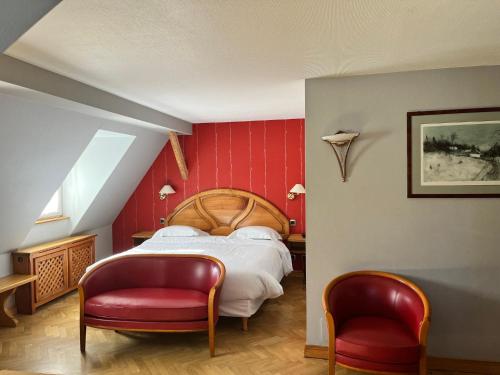 a bedroom with a bed with red walls and two chairs at Logis Hôtel Restaurant Au Cerf d'Or in Strasbourg
