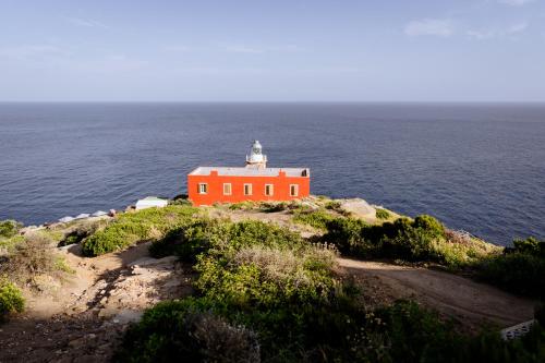 an orange lighthouse on the edge of the ocean at Faro di Punta Fenaio in Campese
