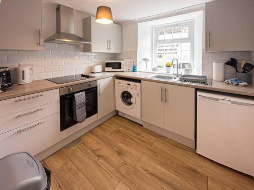 cocina con armarios blancos, fregadero y lavavajillas en Riverview Cottage, en Lanark