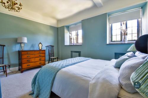 a blue bedroom with a bed and two windows at Poxwell Manor West Wing - Exclusive Dorset Retreat 
