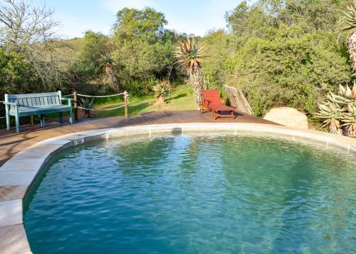 a swimming pool with two chairs and a bench at Stonehill River Lodge by Dream Resorts in Buffeljagsrivier