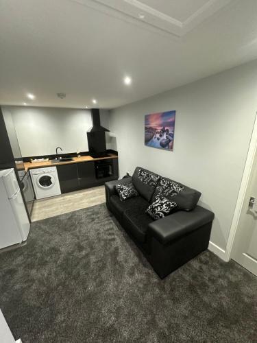 a living room with a black couch and a kitchen at Royal Apartments in Thornaby on Tees