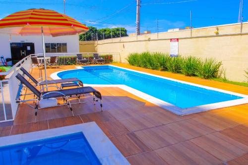 a swimming pool with an umbrella and a chair at Apartamento sofisticado, confortável e bem equipado - Loft Felau in Cuiabá