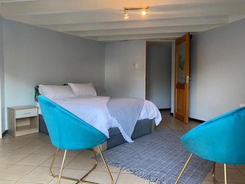 a bedroom with a bed and two blue chairs at Manzi Villa in Hartbeespoort