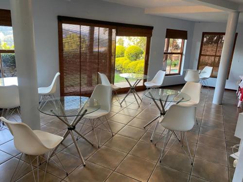 una sala da pranzo con sedie bianche e tavolo in vetro di Manzi Villa a Hartbeespoort