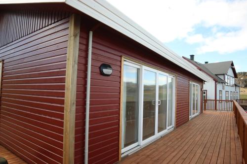 a red building with a deck with windows at Framtid Apartments and Holiday Homes in Djúpivogur