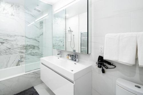 a white bathroom with a sink and a mirror at Stunning 2BD Penthouse in Chelsea w Washer and Dryer in New York