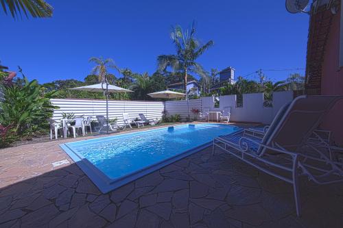 a swimming pool with a chair and a table and chairs at Piscina e 3 dorm. a 150 m de Camburizinho in Camburi
