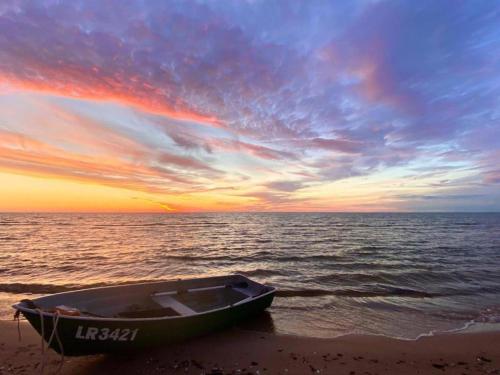 a boat sitting on the beach at sunset at Seaside holiday home Vecvalki in Saunags