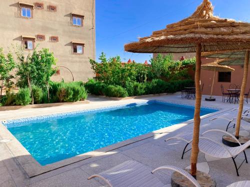 uma piscina com um guarda-sol, uma mesa e cadeiras em Kasbah Tussna em Boumalne