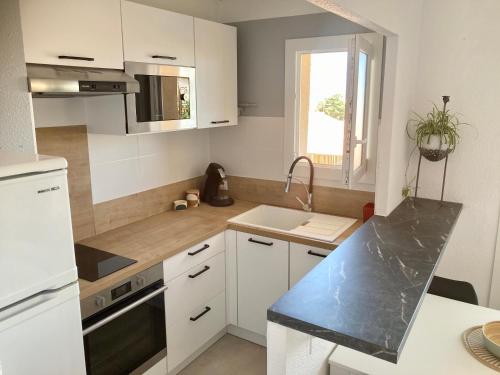 une cuisine avec des armoires blanches, un évier et une fenêtre dans l'établissement Cap au sud !, à Narbonne-Plage