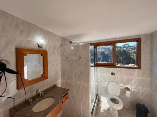 a bathroom with a toilet and a sink and a window at Banyvas Chalés in Monte Verde