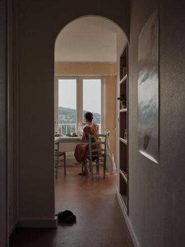 a woman sitting at a table in a room with a window at L'heure Bleue - Meublé de tourisme 3 étoiles in Royat