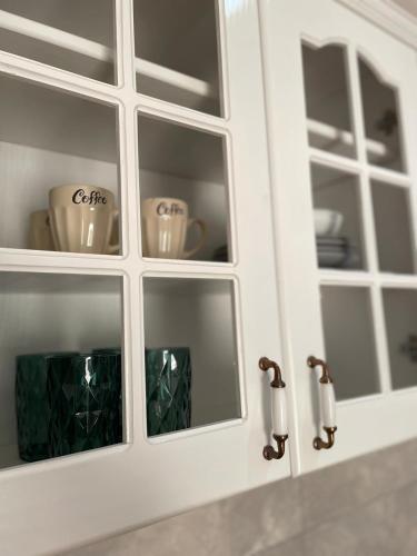 a white cabinet with glass doors with cups in it at Zlatni bor apartmani in Solotuša