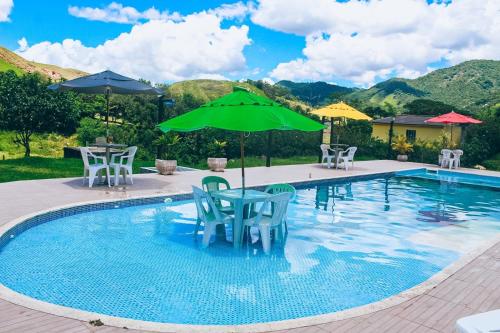 a pool with chairs and umbrellas and a table at Pousada Sítio da Floresta in Sana