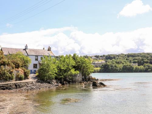 a house on the shore of a river with ducks in the water at Ynys Faelog Cottage in Menai Bridge