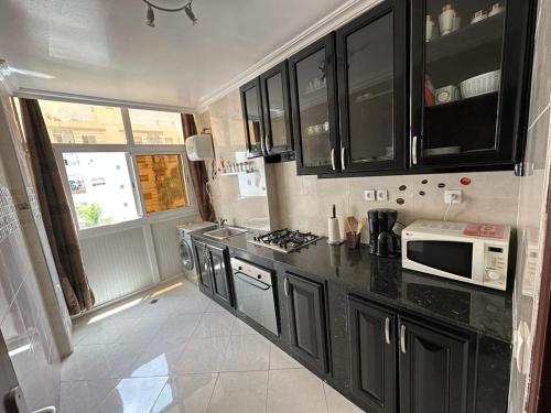 een keuken met zwarte kasten en een magnetron bij Bayti Appart in Agadir