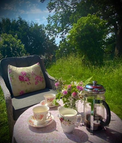 a table with two cups and a jar and flowers at The Old Rectory - Valley View Room In Private Home in Stockton on Teme