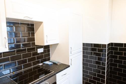 - une cuisine avec du carrelage noir sur le mur et un évier dans l'établissement Gillingham Two bedroom house with garden and free parking, à Gillingham