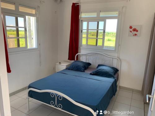 a bedroom with a bed with blue sheets and two windows at Bungalow Little Garden in Mahaudière
