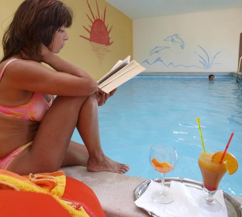 a woman reading a book next to a swimming pool at Hotel Merano in Brenzone sul Garda