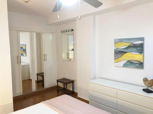a white bedroom with a bed and a painting on the wall at Apartamento Lucía Garden City con piscina climatizada in Playa Fañabe