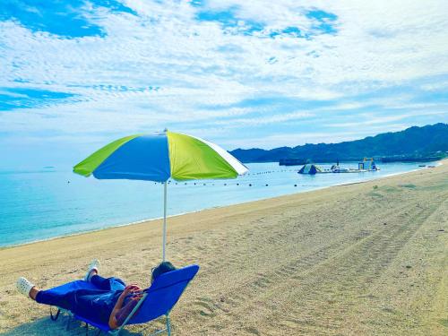 a woman laying in a chair under an umbrella on a beach at なにもない幸せな島のリトリート宿 The Bonds in Matsuyama