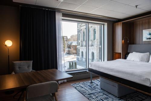 a bedroom with a bed and a desk and a window at Hotel Chicoutimi, affili&eacute; &agrave; Hyvi in Saguenay