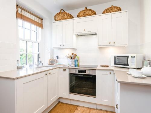a white kitchen with white cabinets and a microwave at Elliot Cottage in Bamburgh