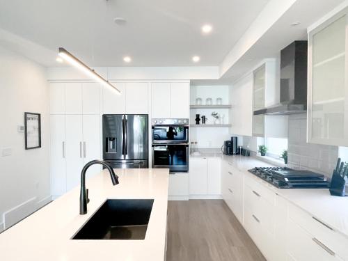 una cocina blanca con armarios blancos y fregadero en *NEW* HAVN HOUSE MODERN RETREAT - STEPS FROM BEACH en Penticton
