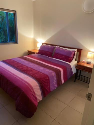 a bedroom with a bed with purple sheets and a window at Mauna Loa Apartment in Darwin