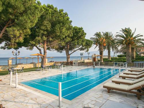 a swimming pool with chairs and trees and the ocean at Nefeli Studios in Erateini