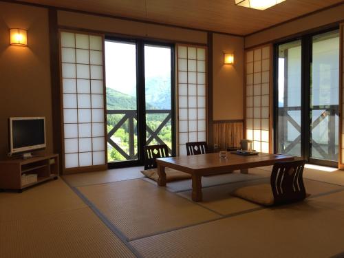 a room with a table and a television and windows at Yufuin Tsubaki in Yufuin