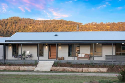 a white house with a porch and mountains in the background at The House - The Charles at Broke Hunter Valley Luxury in Broke