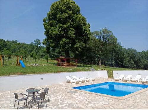 uma piscina com cadeiras, uma mesa e um parque infantil em Farma & Apartmani OPG Sasa Delic em Korenica