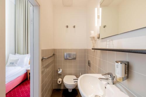 ベルリンにあるノヴム ホテル ゲイツ ベルリン シャルロッテンブルクのバスルーム(洗面台、トイレ付)、ベッド1台が備わります。