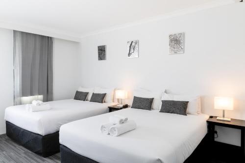 Joondalup City Hotel في بيرث: سريرين في غرفة الفندق ذات شراشف بيضاء