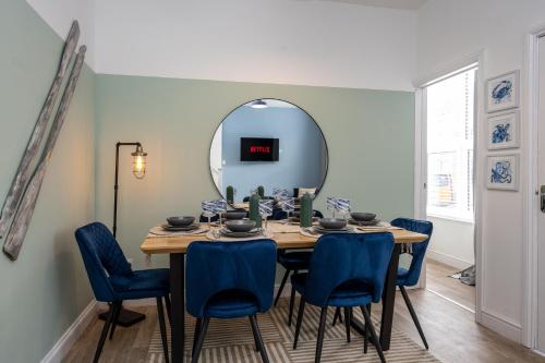 a dining room table with blue chairs and a mirror at Spacious 4BR Home with outdoor seating in Swansea in Swansea