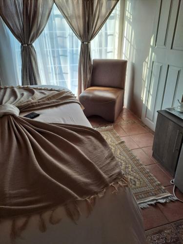 a bedroom with a bed and a chair and a window at Courtlyguesthouse in Witbank