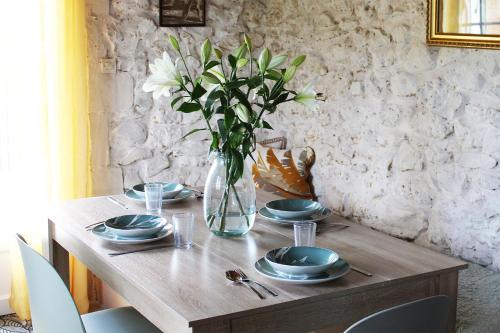 a wooden table with plates and a vase with flowers at Les Rocailles in Lamonzie-Montastruc