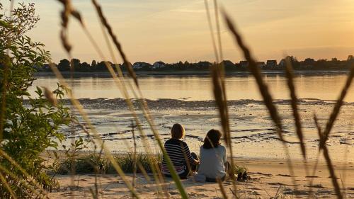 two women sitting on the beach looking at the water at FEWO Morgenröte - Weserblick -Harriersand in Schwanewede