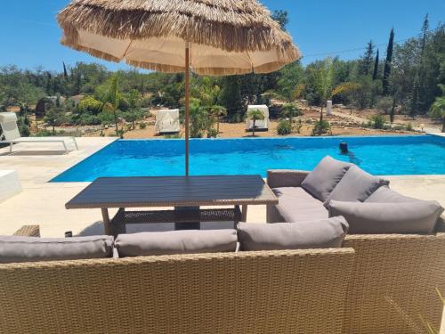 a table with chairs and an umbrella next to a swimming pool at Villa das Alfarrobas Cosy Guest House in Algoz
