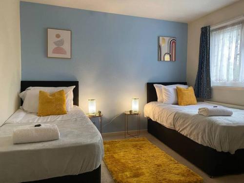 a bedroom with two beds with yellow pillows and a rug at Comfortable 3 bed House - Great Monthly Discounts in Worting