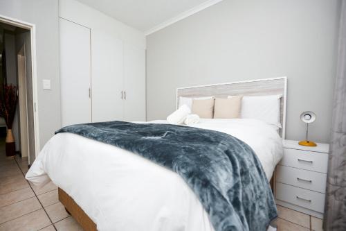 a bedroom with a white bed with a blue blanket on it at Cosy Hatfield Apartment in Pretoria