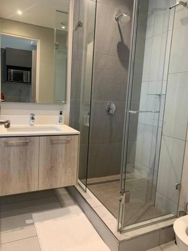 a bathroom with a glass shower and a sink at Entire Studio Apartment @MenlynMaine in Pretoria