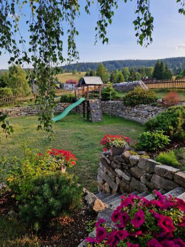un jardín con un parque infantil con flores y una pared de piedra en Pension MAX en Pernink